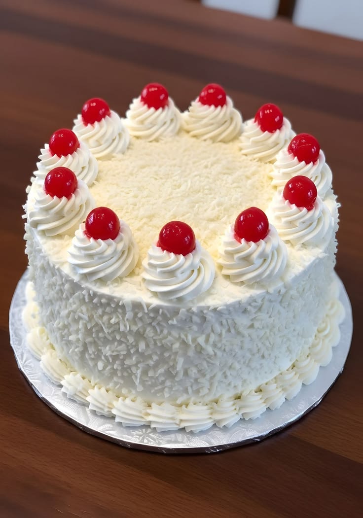 Bolo branco de coco decorado com chantilly e cerejas vermelhas